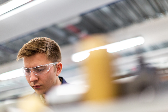 Junger Mitarbeiter mit Sicherheitsbrille in Produktion